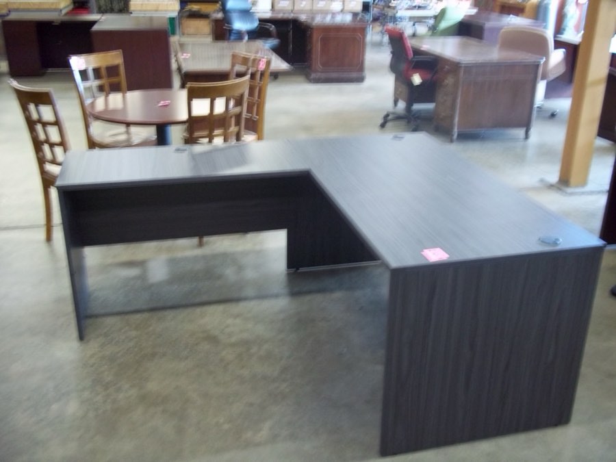 A grey laminate L-shaped desk on the Hull Street Outlet office furniture floor, with wood chairs and used desks behind it.