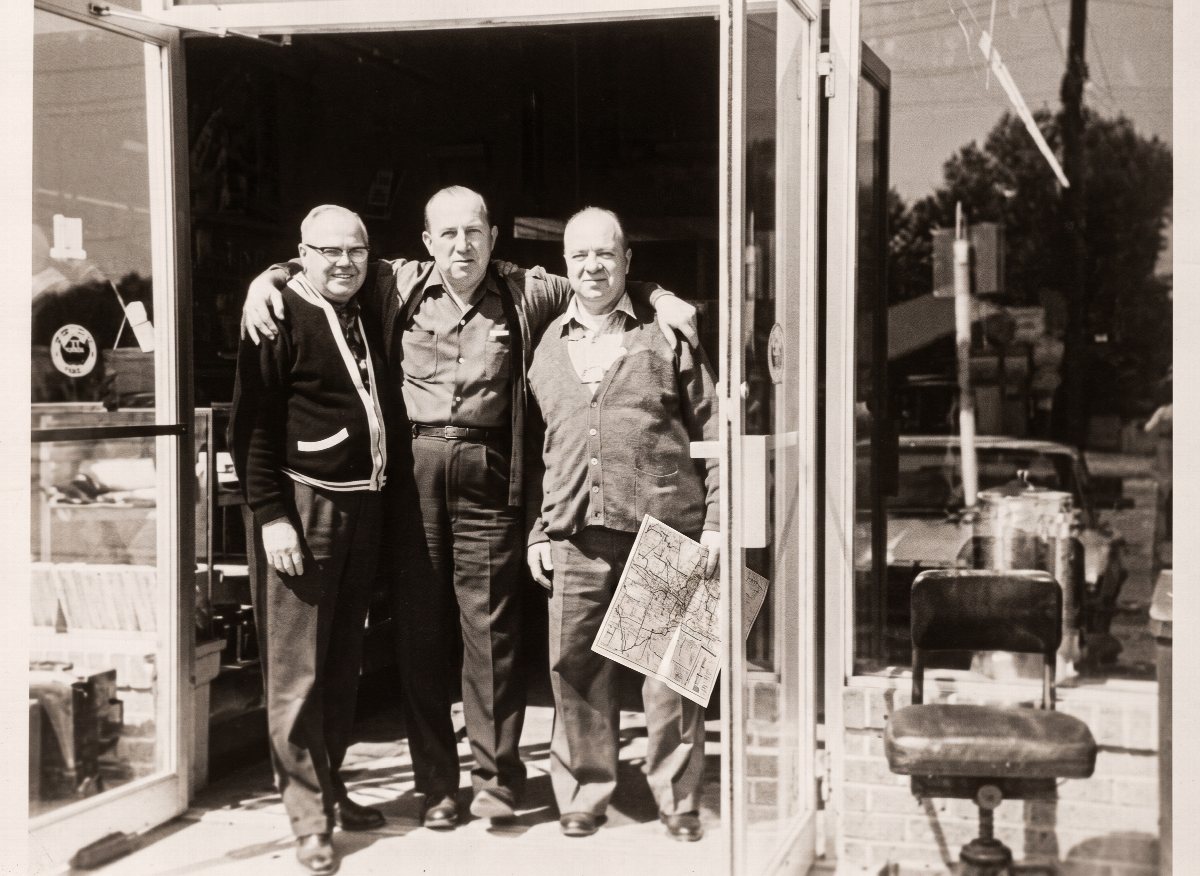 Black and white photograph from 1965 of Sam Finn standing with two colleagues in the doorway of the Hull Street Outlet store.