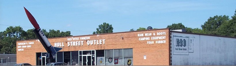 The Hull Street Outlet storefront: a long brick building with the store name painted across the front and a tall red-tipped rocket standing beside the entrance.