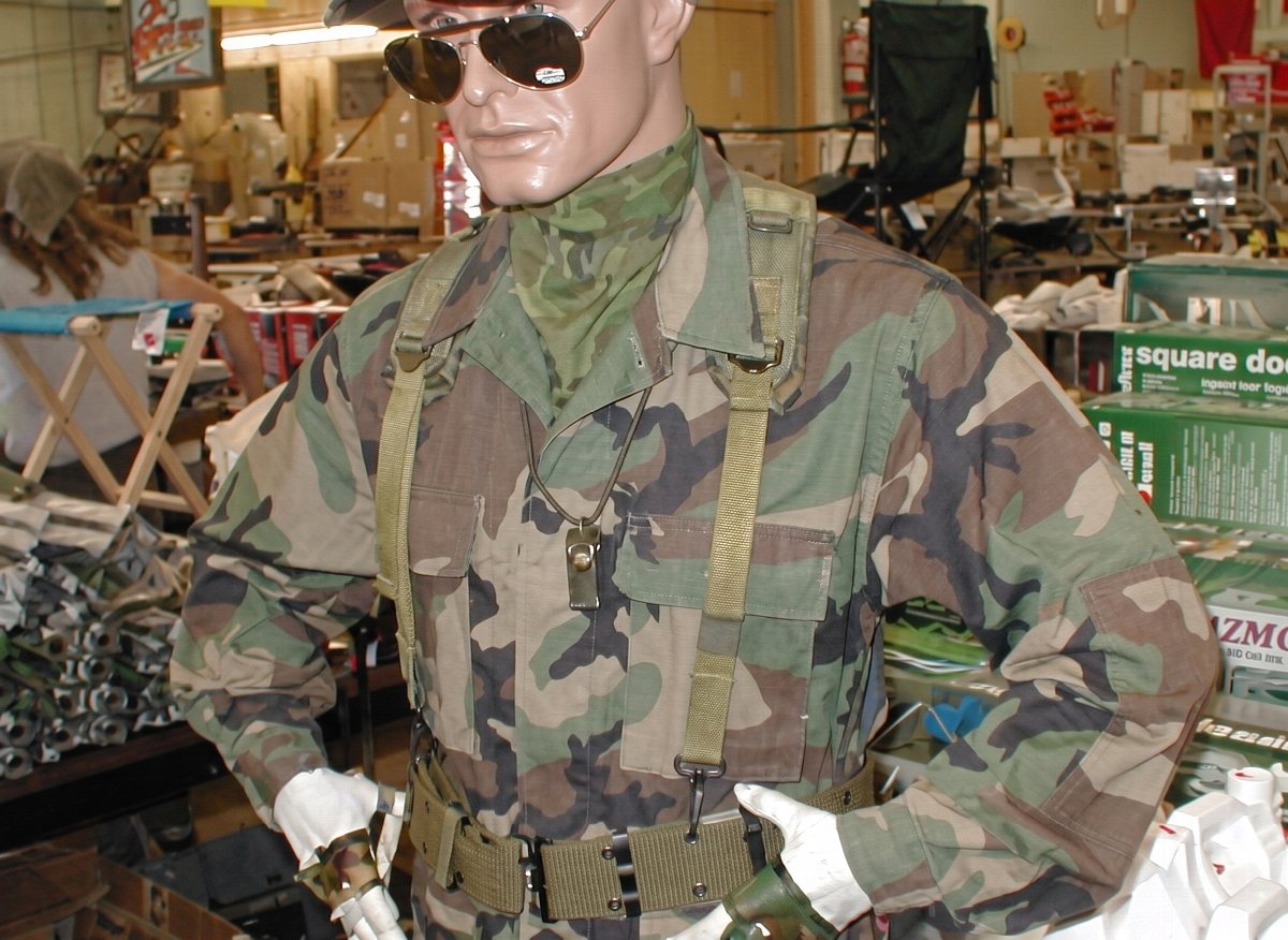 A mannequin outfitted in woodland camouflage BDUs with load-bearing webbing and a boonie hat on the surplus sales floor.